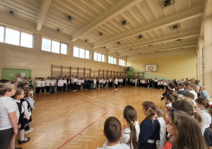 Uczniowie i nauczyciele śpiewają hymn na sali gimnastycznej