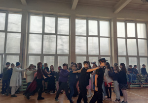 Uczniowie tańczą trzymając się za ramiona.