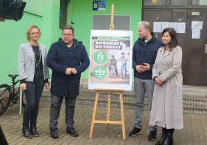 Goście i dyrekcja stoją wokół plakatu